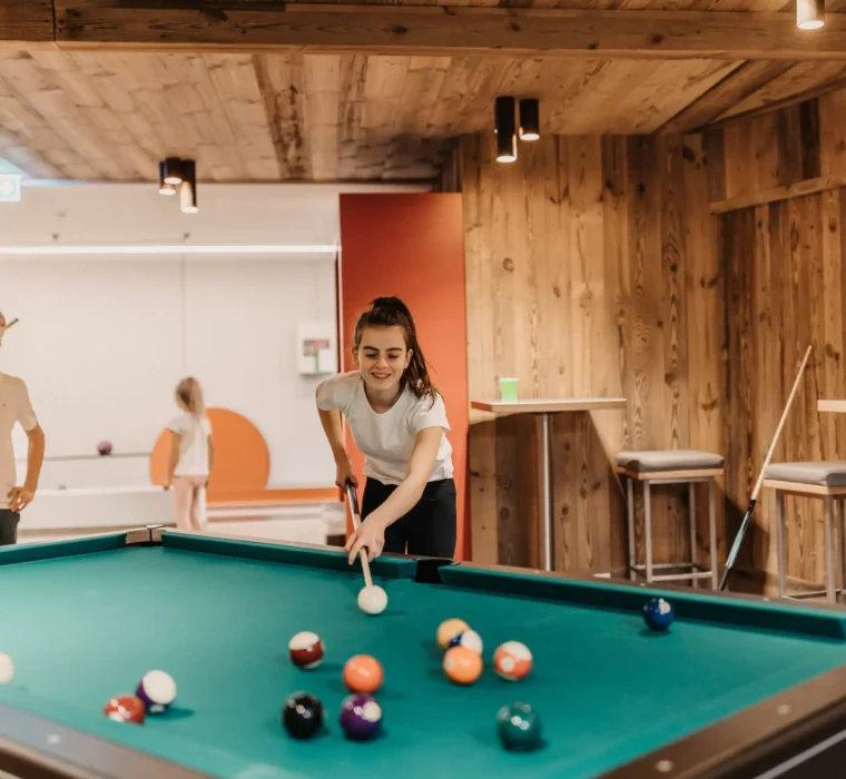 Spielspaß für Groß und Klein: Familienzeit am Billardtisch in der stylischen Games Area des Hofgut Wagrain – gemeinsam lachen, zielen und genießen.