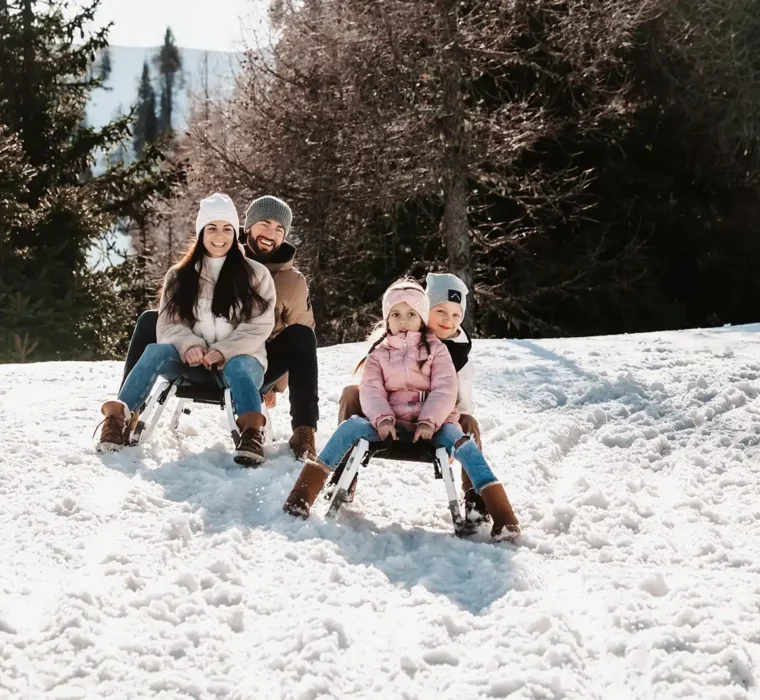 Family tobogganing on a snowy slope, laughing and wearing winter clothing.