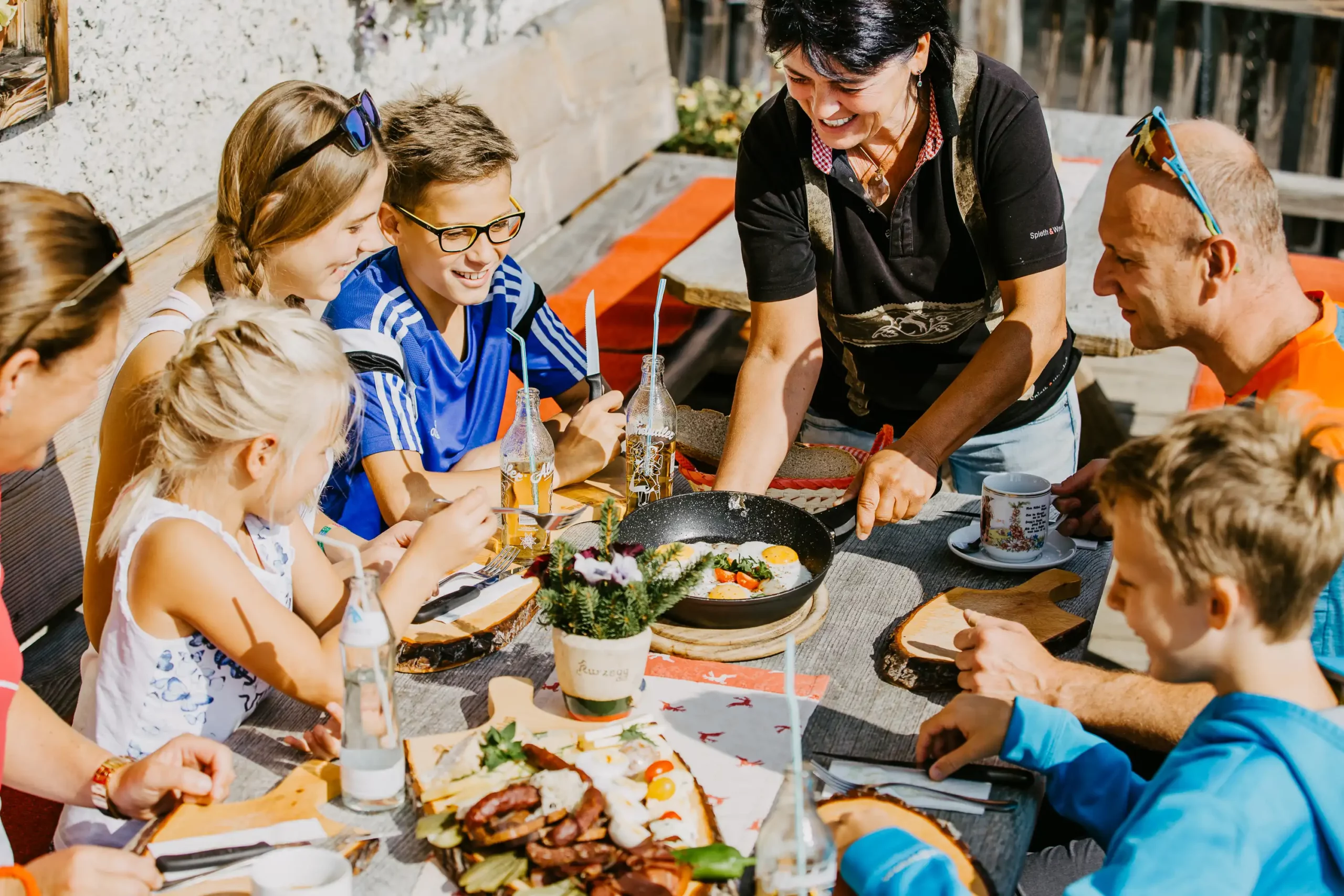 A cheerful family enjoying a savoury snack with fried eggs in a sunny mountain hut - genuine hospitality and regional delights in Salzburger Land.