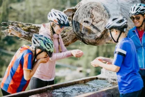 Familie erfrischt sich an einer urigen Bergquelle während ihrer Radtour – kristallklares Quellwasser, lachende Gesichter und ein unvergesslicher Moment in der Salzburger Natur.