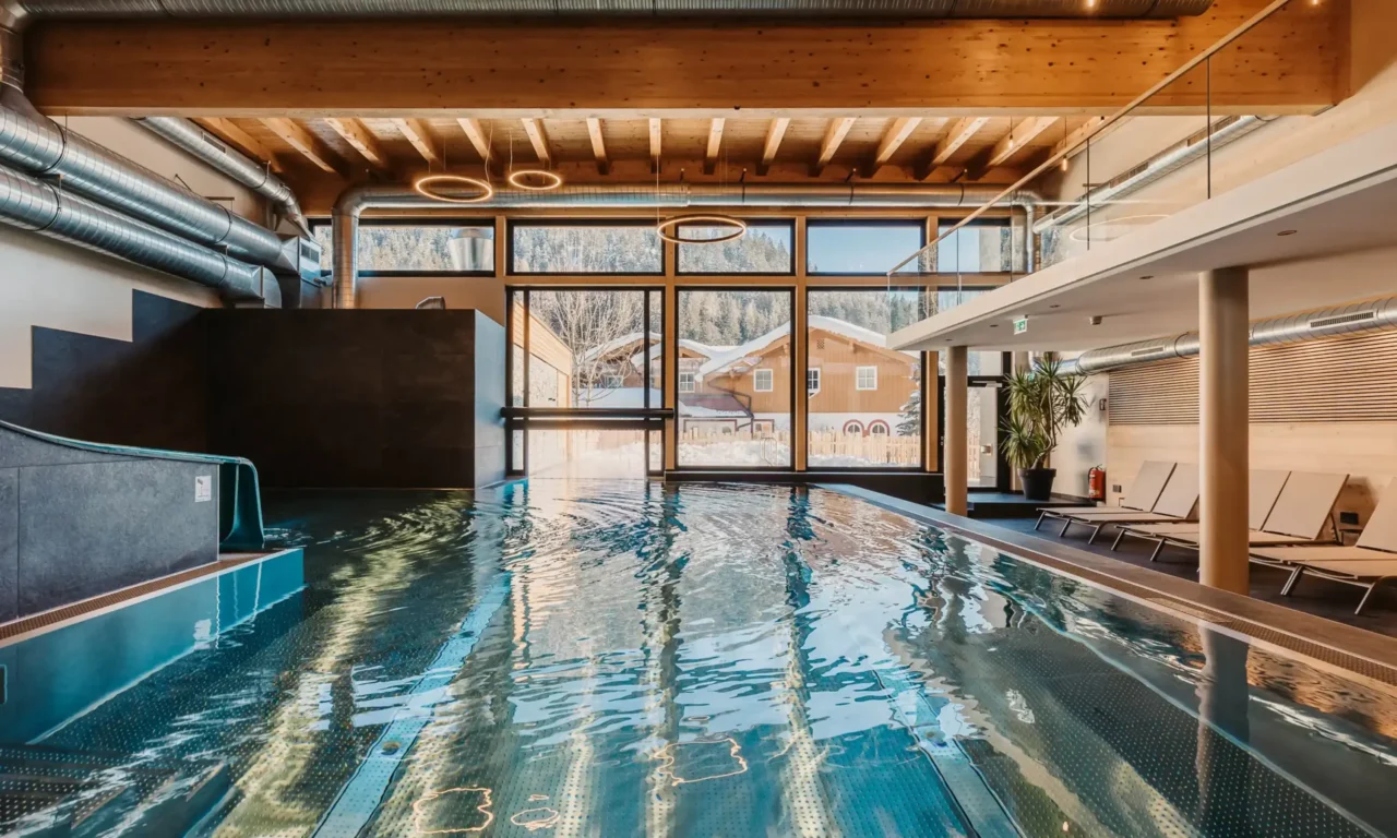 Atmospheric shot of the indoor pool at Hofgut Wagrain with a view of the snow-covered valley – soothing warmth, modern design, and a unique place to pause and reflect.
