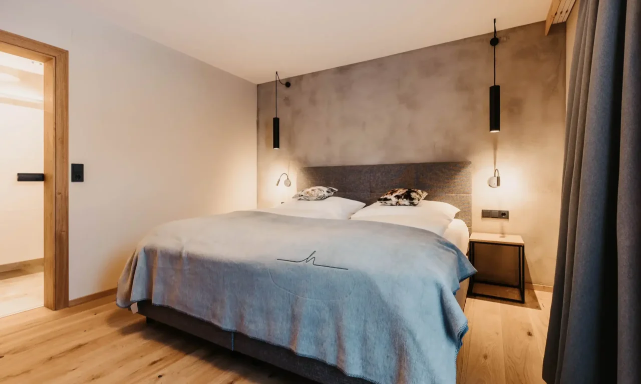 Cosy bedroom with modern box-spring bed, minimalist lighting, wooden flooring and soft natural tones - stylish design with alpine flair.