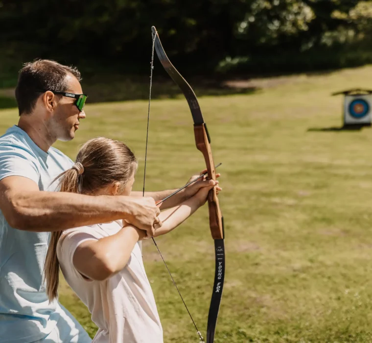 Aiming for the target on holiday - joint archery for children and adults on the meadow in the sunshine.