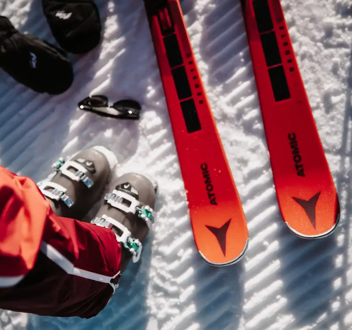 Detailaufnahme von Skischuhen und Atomic-Ski auf der Piste im frischen Schnee.