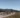 A family rides their bikes on a gravel track through a mountain landscape with lush meadows and forests.