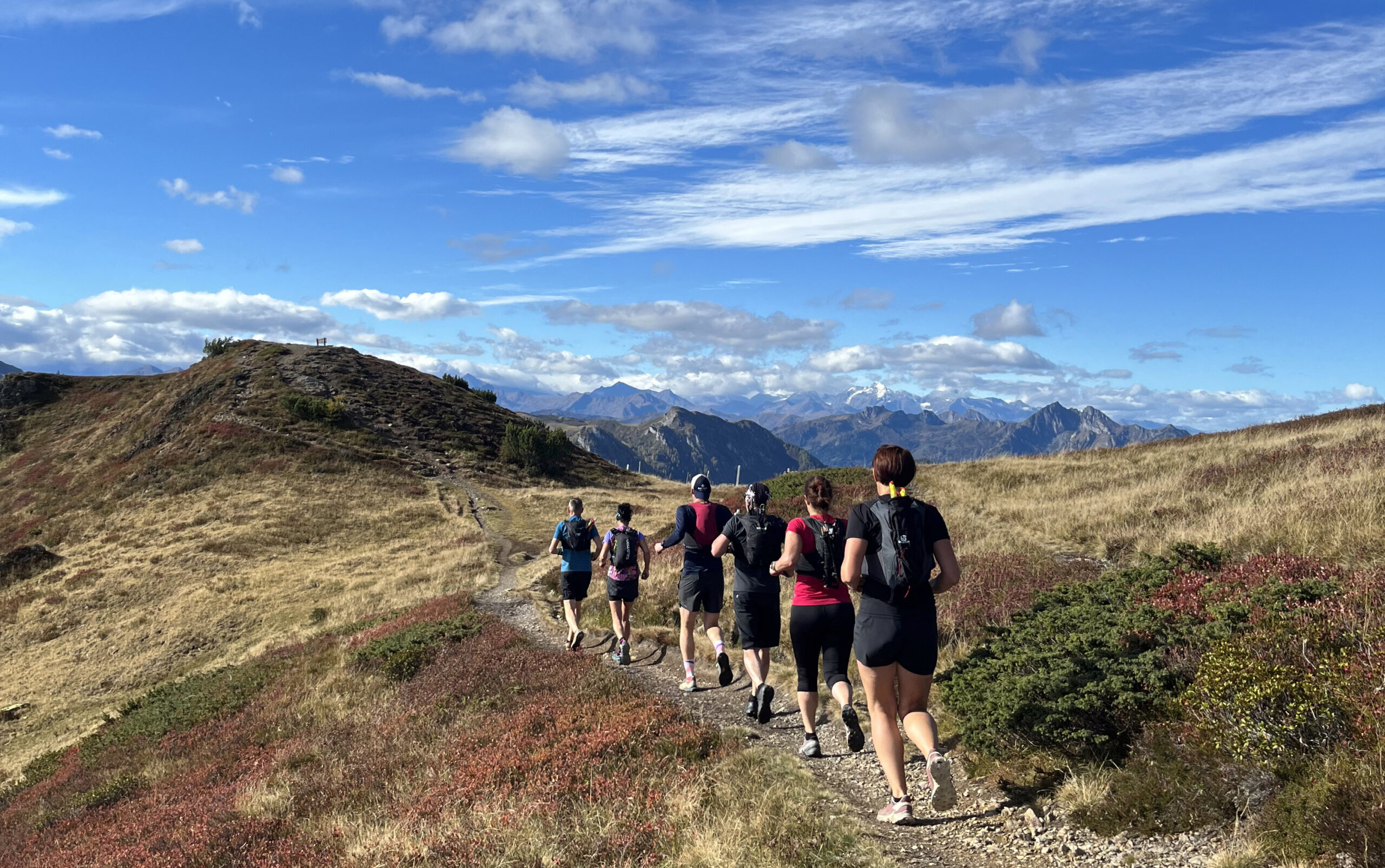 Trail running met uitzicht - loopgroep op een panoramisch hooggelegen pad in de bergen van Salzburg, omgeven door gouden alpenweiden, herfstachtige natuur en een indrukwekkend alpenpanorama.