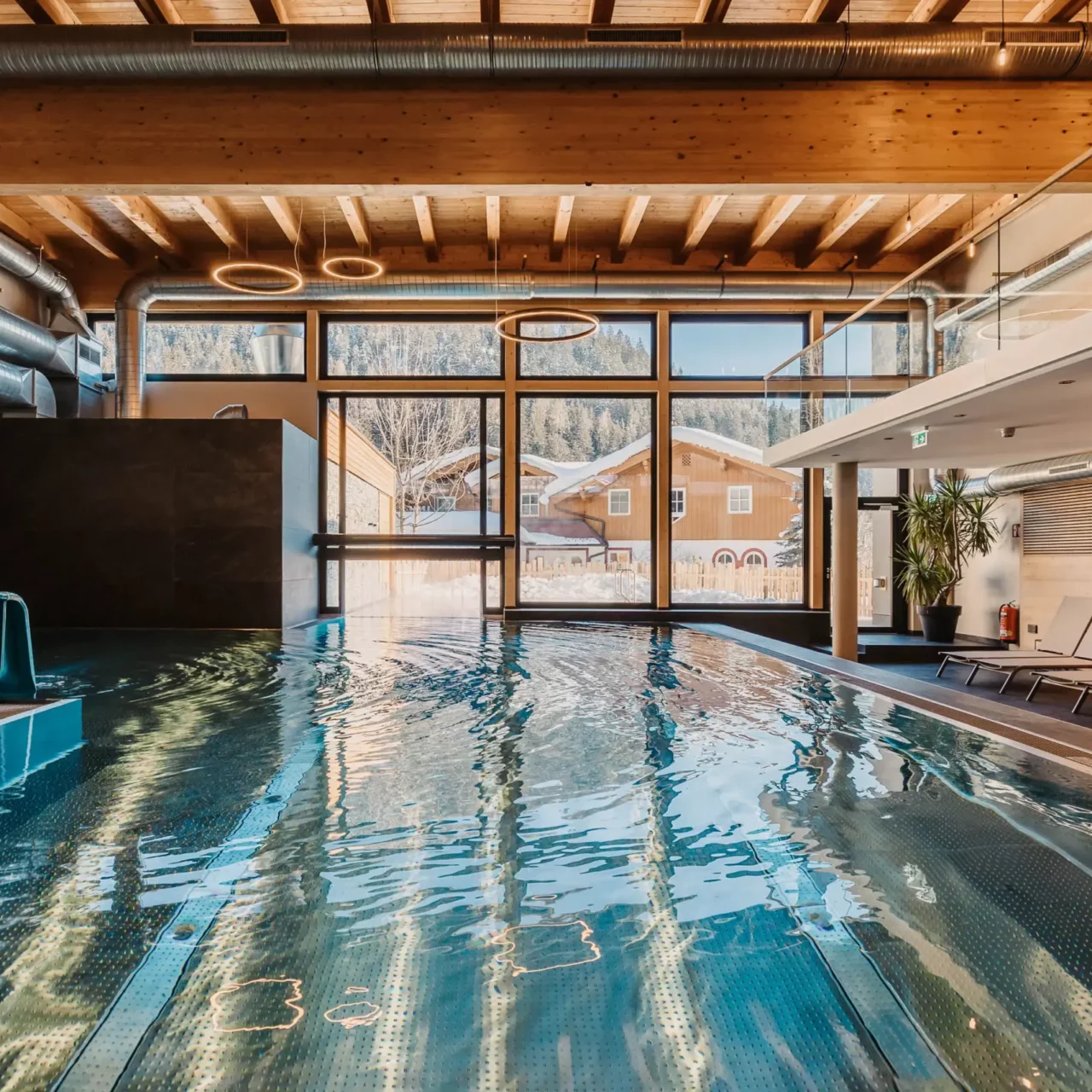Atmospheric shot of the indoor pool at Hofgut Wagrain with a view of the snow-covered valley - cosy warmth, modern design and a unique place to pause for a moment.