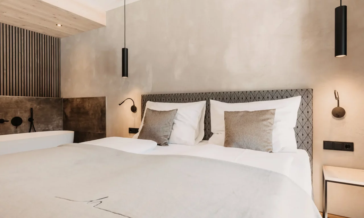 Elegant bedroom at Hofgut Wagrain with box-spring bed, modern lamps and free-standing bathtub.