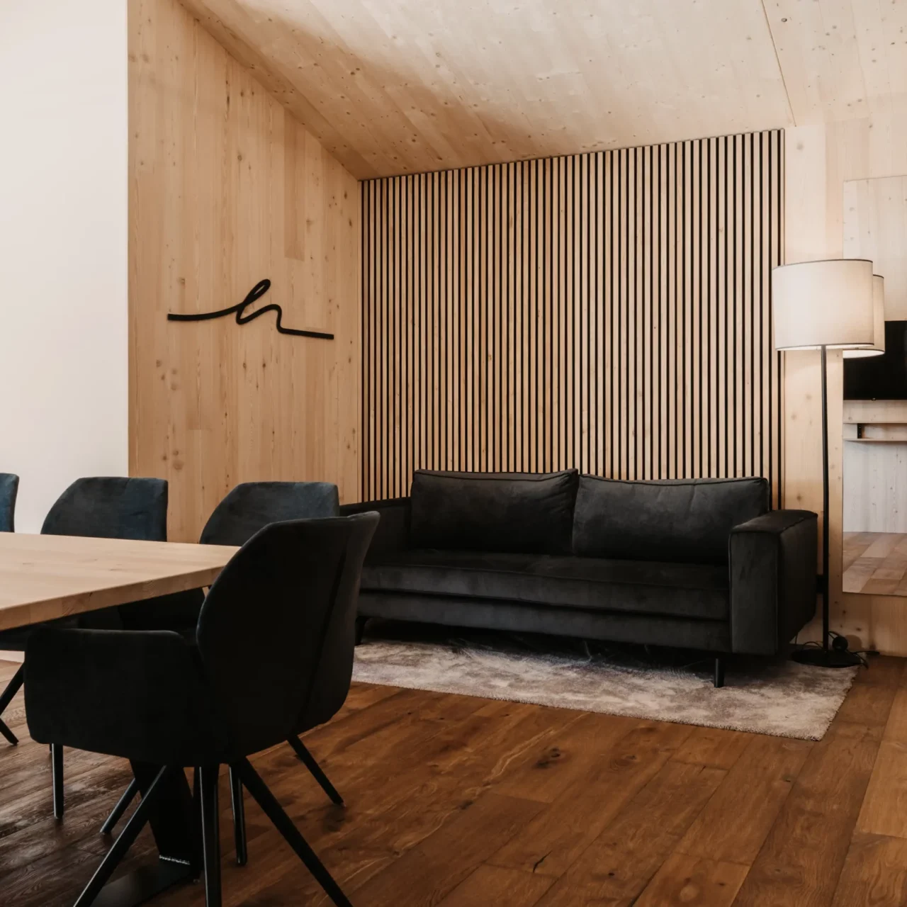 Cosy living area at Hofgut Wagrain: elegant sofa in front of stylish wood panelling, warm lighting accents and modern interior for relaxed family moments in an alpine ambience.
