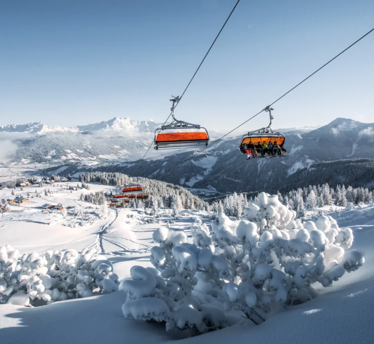 Ski lift with orange weather protection bonnets in the snow-covered Flachau ski area with a view of the Alps.