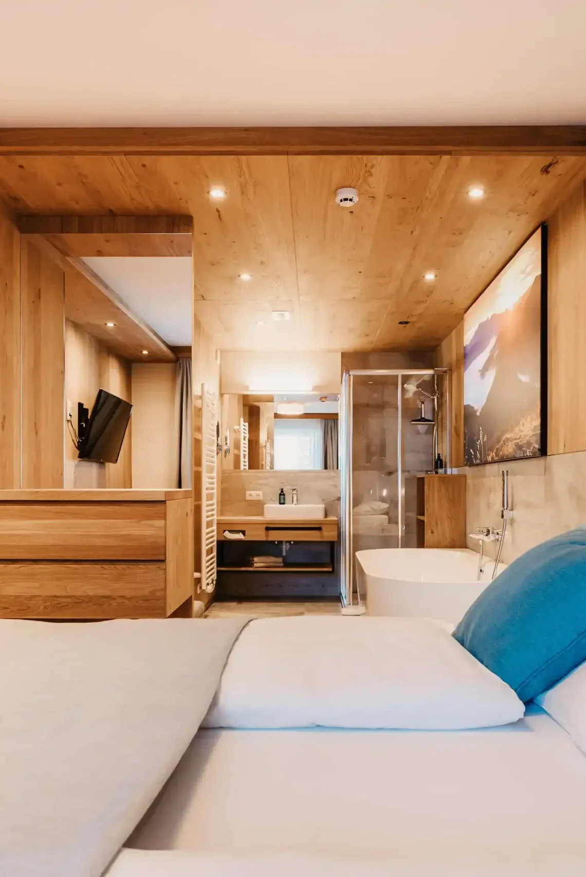 Modernes Schlafzimmer im Hofgut Wagrain mit Doppelbett, freistehender Badewanne und offenem Badbereich in hellem Holzdesign.