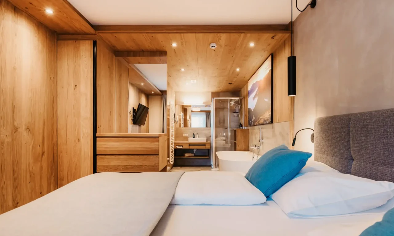 Modernes Schlafzimmer im Hofgut Wagrain mit Doppelbett, freistehender Badewanne und offenem Badbereich in hellem Holzdesign.