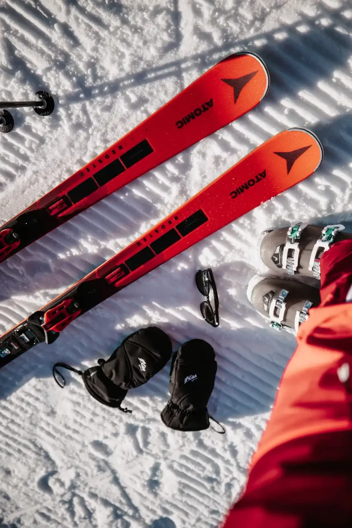 Skiudstyr på sne, røde ski, sorte handsker, sorte solbriller, grå skistøvler.