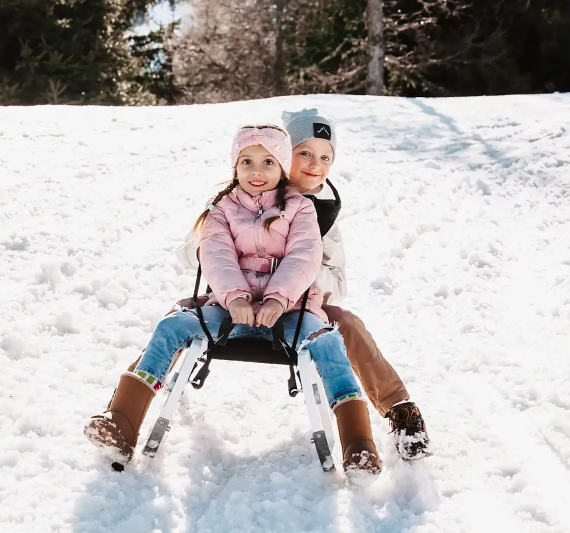Kinder fahren mit der Rodel die Rodelbahn von der Kleinarlerhütte hinunter.