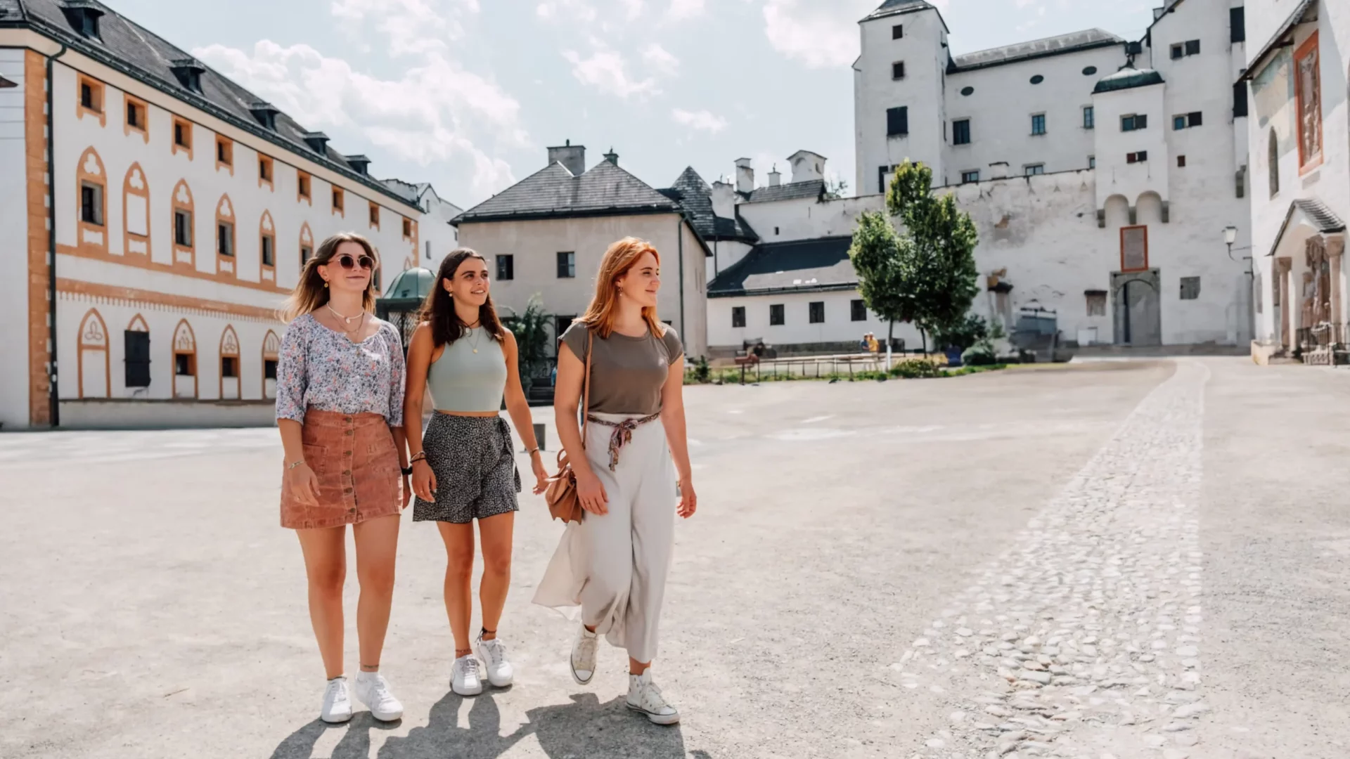 Three young women explore a historic old town in the Salzburg region in the sunshine during their holiday