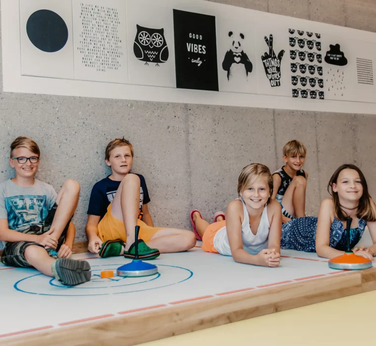 Hofgut-Wagrain-Apartment-Lifestyle-Resort-Erleben-im-Hofgut-für-Kinder-Stockbahn Children playing curling in the indoor games area at Hofgut Wagrain.