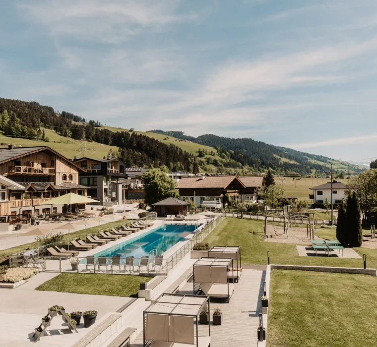 Sunny summer view of the outdoor pool and garden area of Hofgut Wagrain with a panoramic view of the Alps