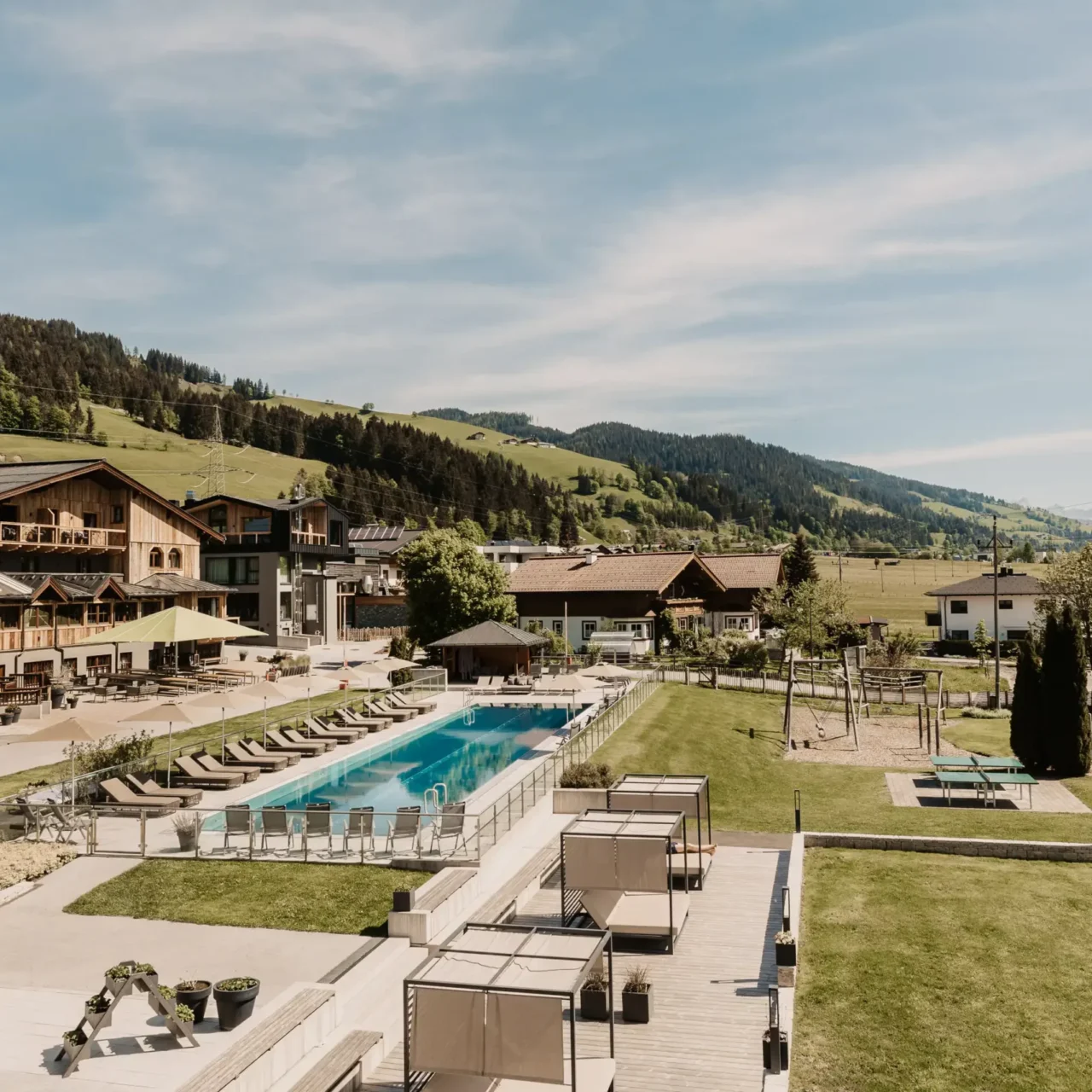 Zonnig zomeruitzicht op het buitenzwembad en de tuin van Hofgut Wagrain met een panoramisch uitzicht op de Alpen