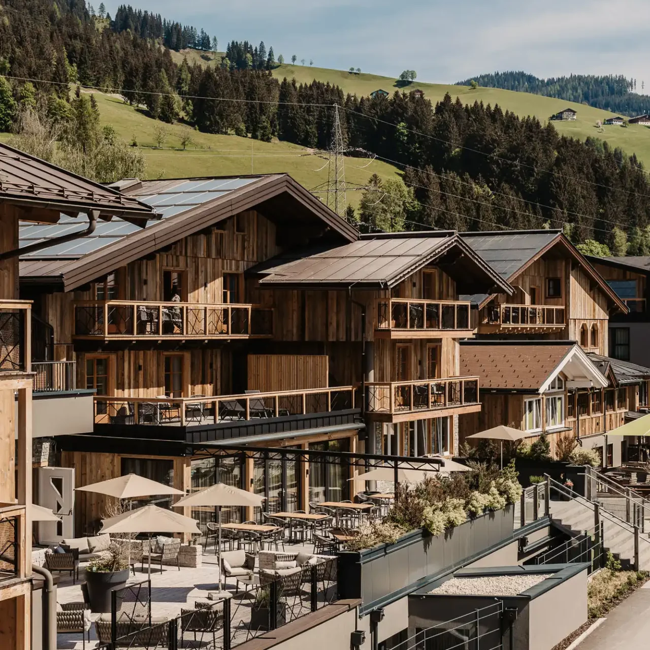 Exterior view of Hofgut Wagrain with sun terrace and modern Alpine architecture in front of a green hilly landscape