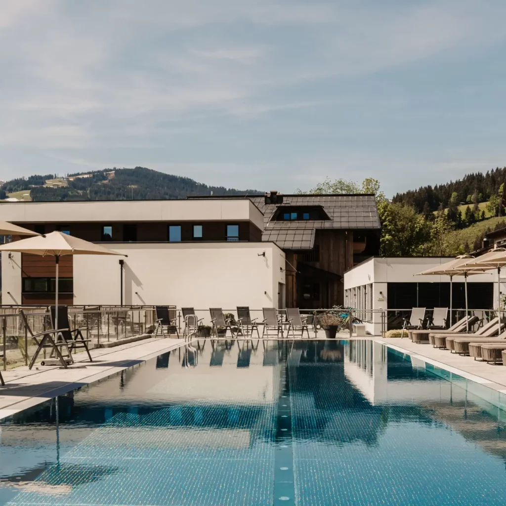 25-Meter-Sportbecken im Hofgut Wagrain mit Sonnenliegen und Schirmen – Sommerliche Ruheoase mit Bergblick für aktive und entspannte Urlaubstage im Salzburger Land.