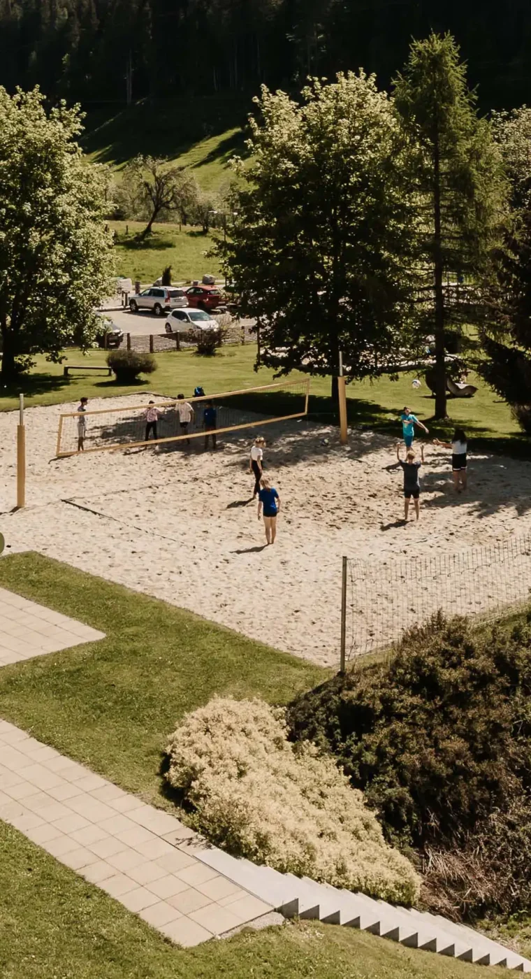 Gäste spielen Beachvolleyball im Hofgut Wagrain umgeben von Bäumen und Bergpanorama