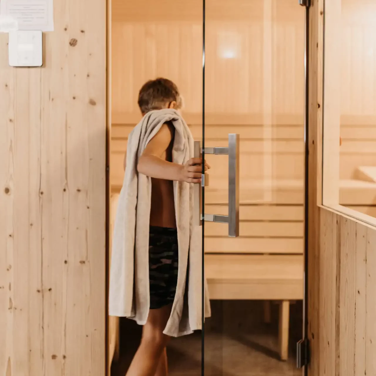 Ein Junge steht mit einem Handtuch vor der familienfreundlichen Textilsauna im Hofgut Wagrain – entspannte Wellnessmomente auch für junge Gäste.