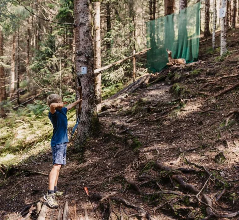Junge übt Bogenschießen im 3D-Parcours im Wald beim Hofgut Wagrain