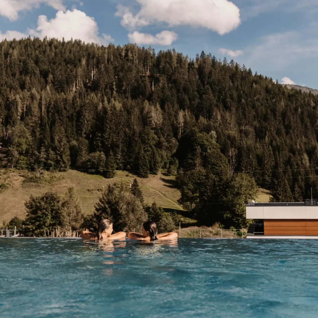 Zwei Gäste genießen den Moment im Infinity-Pool des Hofgut Wagrain – mit atemberaubendem Blick auf die umliegenden Berge und Wälder. Pure Entspannung und alpines Lebensgefühl vereint an einem ganz besonderen Ort.