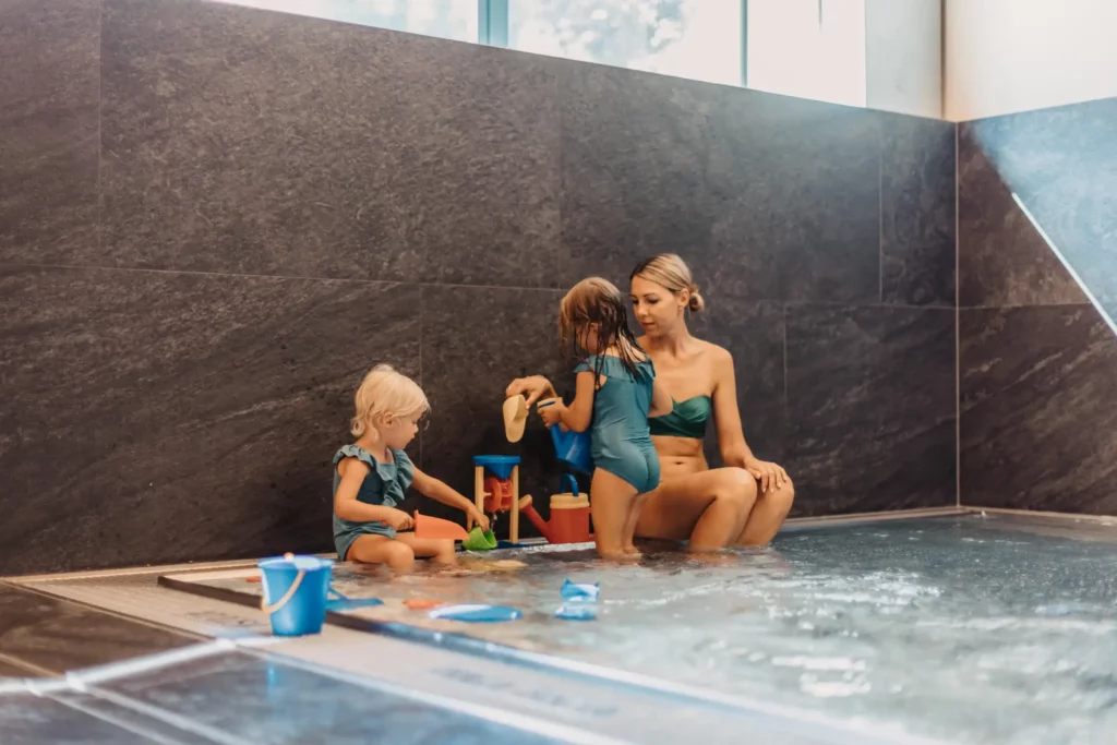 Playtime together in the baby pool - a mother and her two little daughters enjoy the relaxed atmosphere in the warm water area at Hofgut Wagrain, surrounded by loving details and child-friendly water toys.