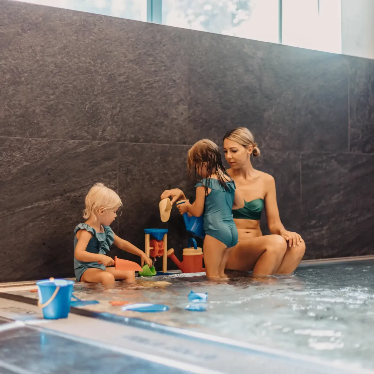 Gemeinsame Spielzeit im Babypool – eine Mutter genießt mit ihren beiden kleinen Töchtern die entspannte Atmosphäre im warmen Wasserbereich des Hofgut Wagrain, umgeben von liebevollen Details und kindgerechten Wasserspielsachen.
