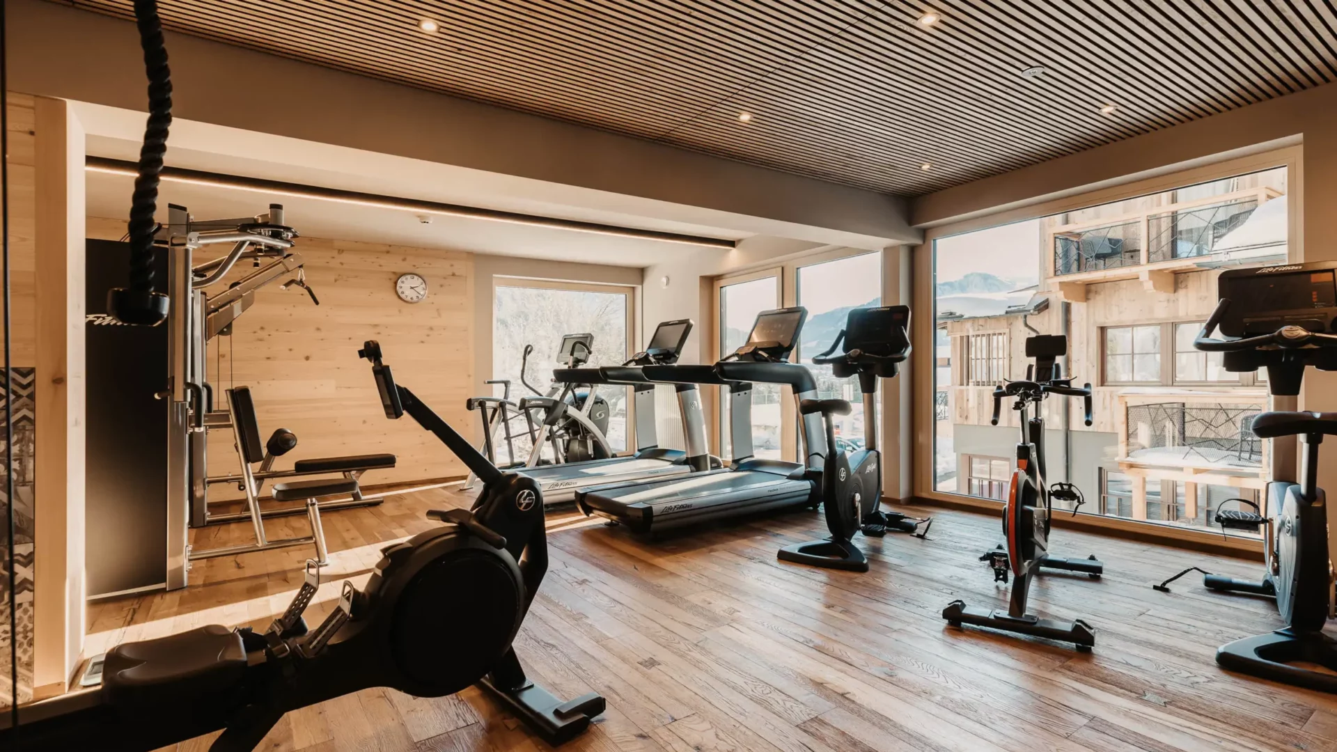 Modernes Fitnessstudio im Hofgut Wagrain mit hochwertigen Geräten, Holzdesign und Blick auf die verschneiten Berge.