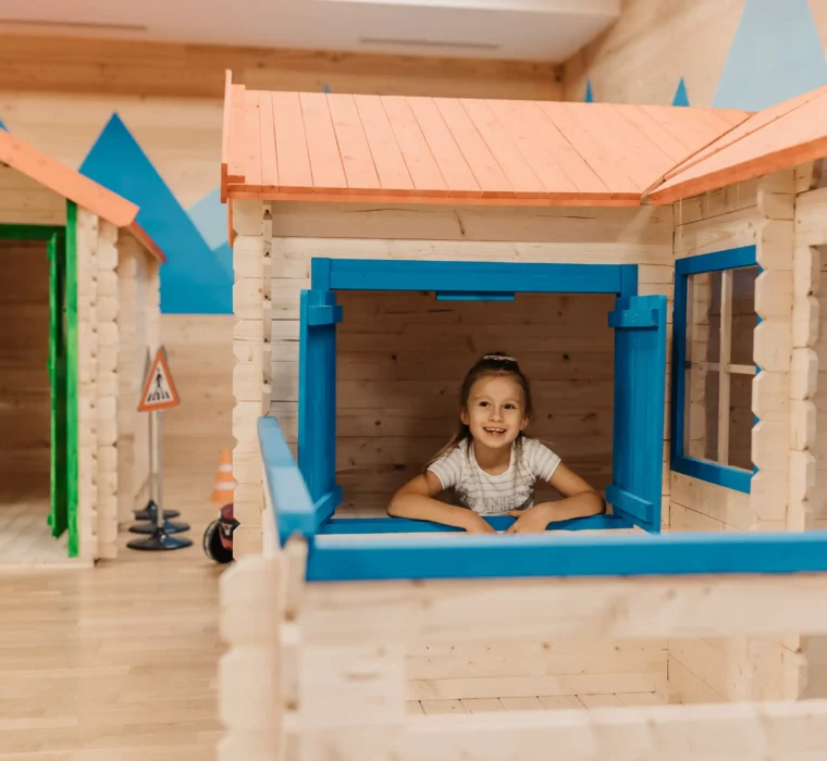 Playful discovery in the Mini Park: A cheerful girl looks out of the window of a lovingly designed playhouse at Hofgut Wagrain - a place full of fantasy, adventure and childlike joy.