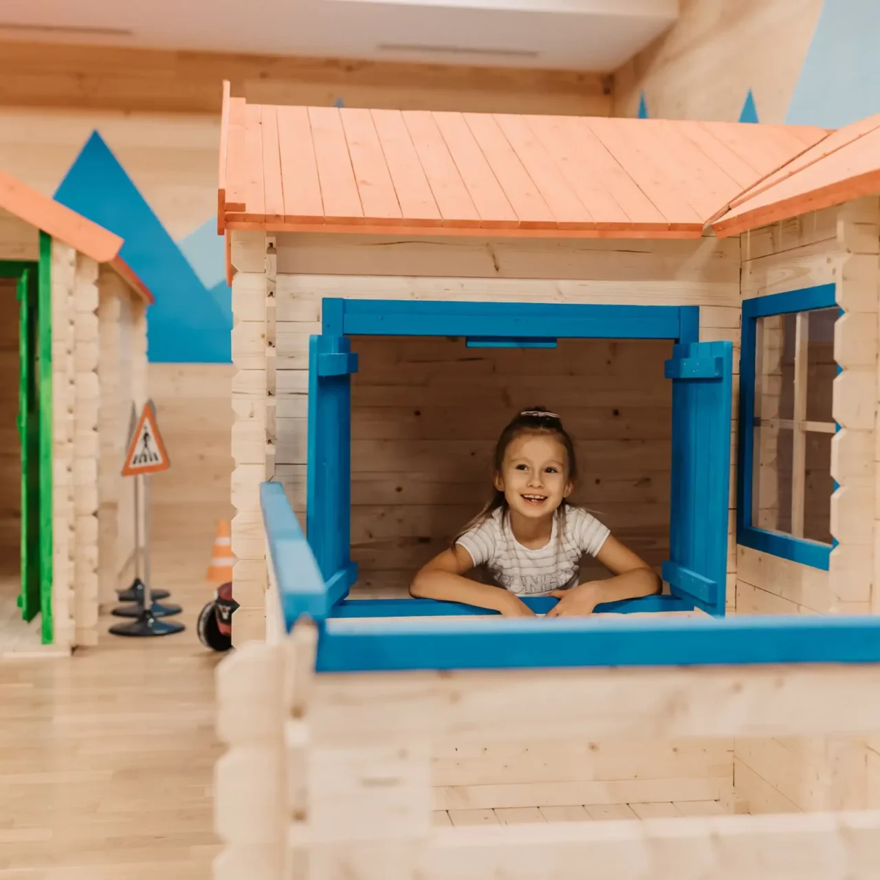 Playful discovery in the Mini Park: A cheerful girl looks out of the window of a lovingly designed playhouse at Hofgut Wagrain - a place full of fantasy, adventure and childlike joy.