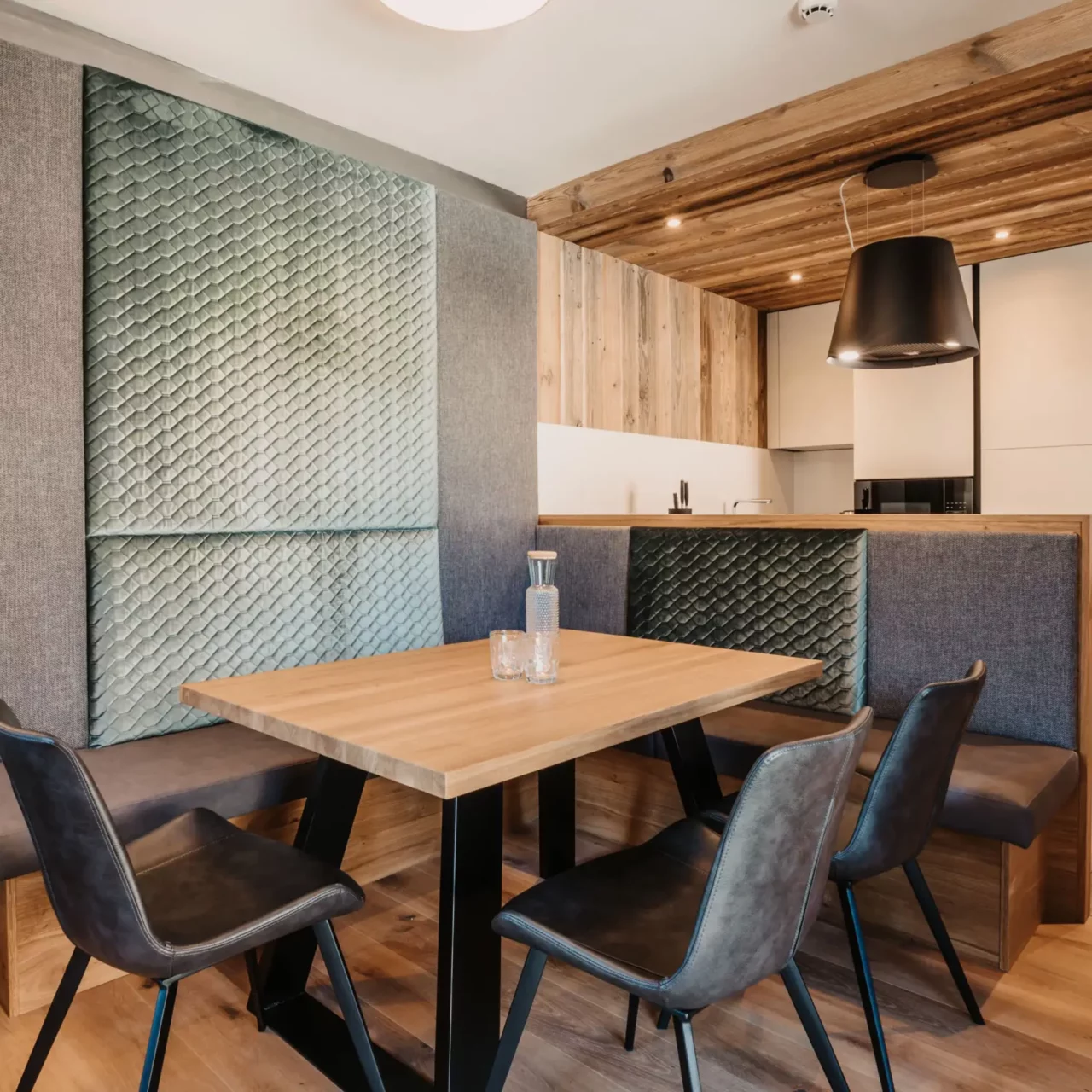 Cosy dining and eat-in kitchen at Hofgut Wagrain with modern wood panelling, stylish bench with back cushions, elegant dining table and atmospheric lighting design.