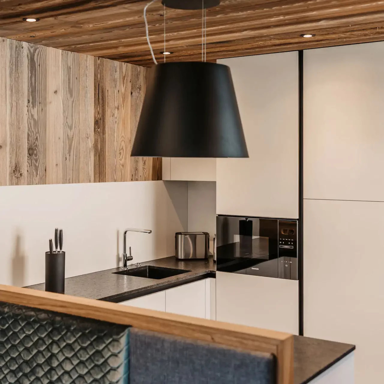 Stylish kitchen with wooden ceiling, black extractor bonnet and minimalist furnishings.