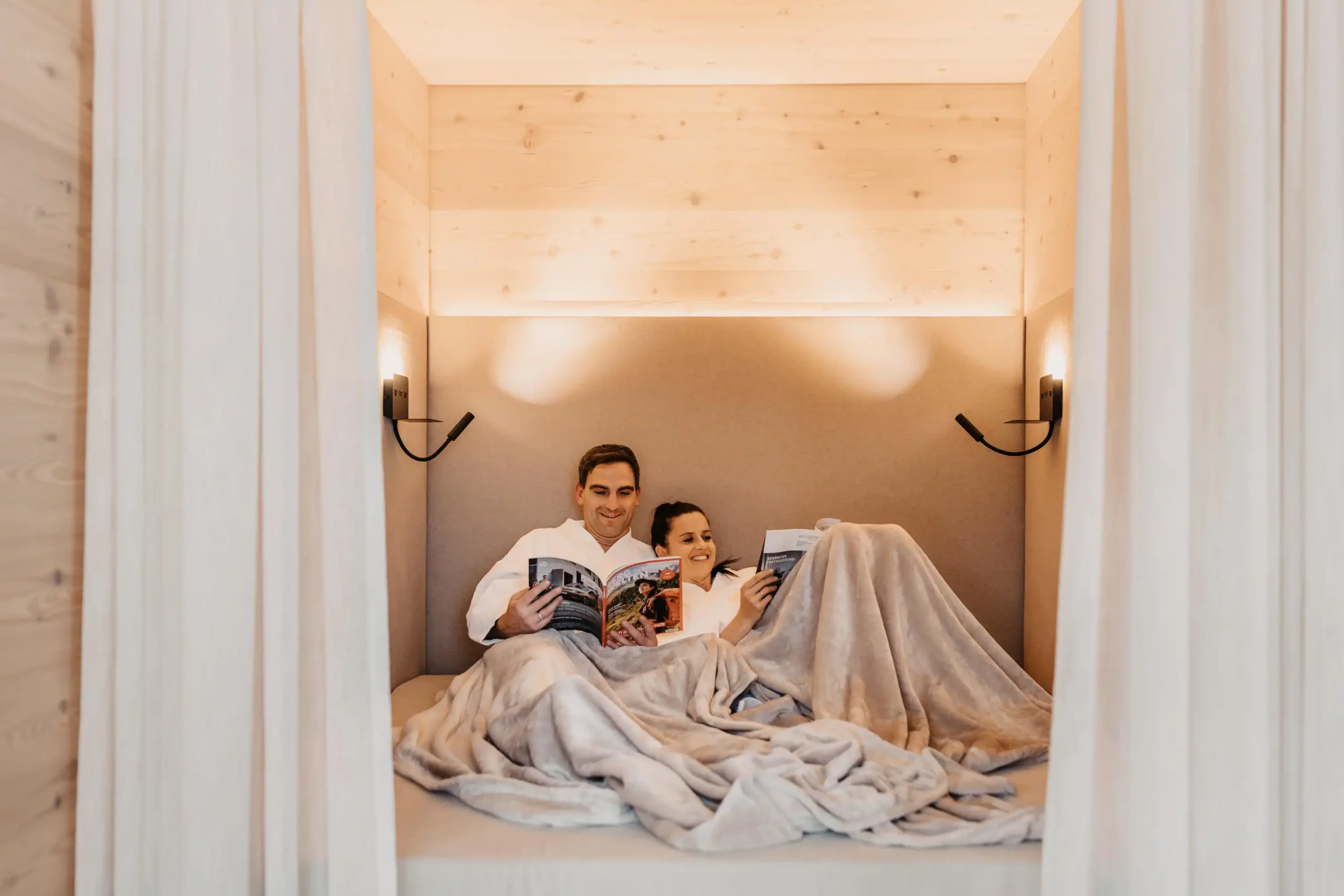 Hofgut-wagrain-apartment-269 Couple relax and read magazines in an alcove furnished with blankets.