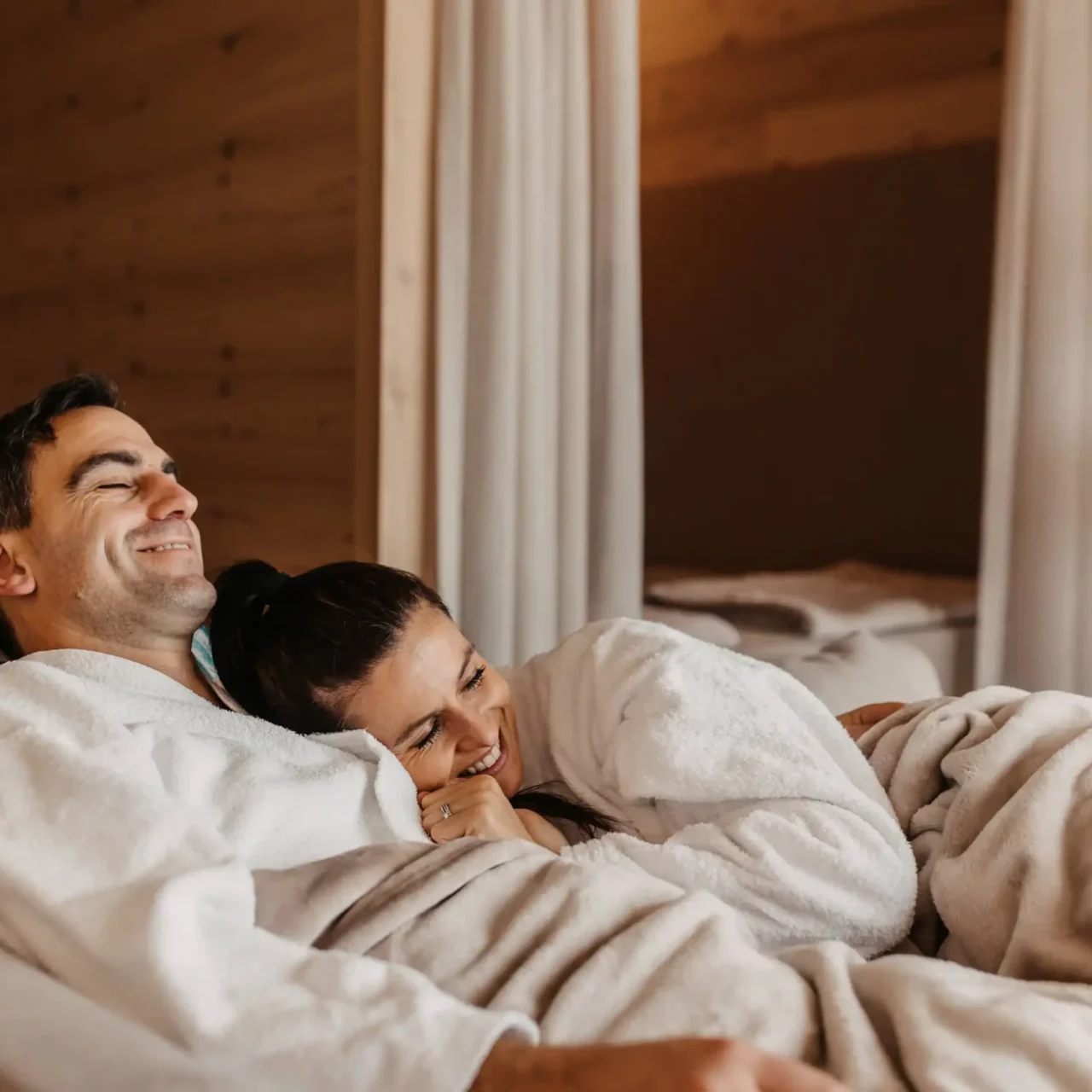 Enjoy togetherness at Hofgut Wagrain - a relaxed couple wrapped up in fluffy bathrobes on a cosy lounger in the relaxation room. The warm wooden look and cosy atmosphere make this moment unforgettable.
