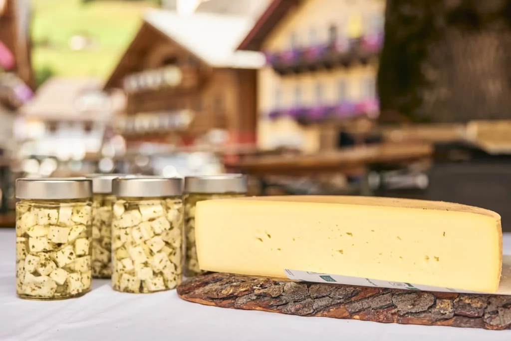 Regionale Käseköstlichkeiten aus dem Salzburger Land: frischer Schnittkäse und würziger Kräuter-Schafkäse im Glas – präsentiert vor traditioneller Alpenkulisse.