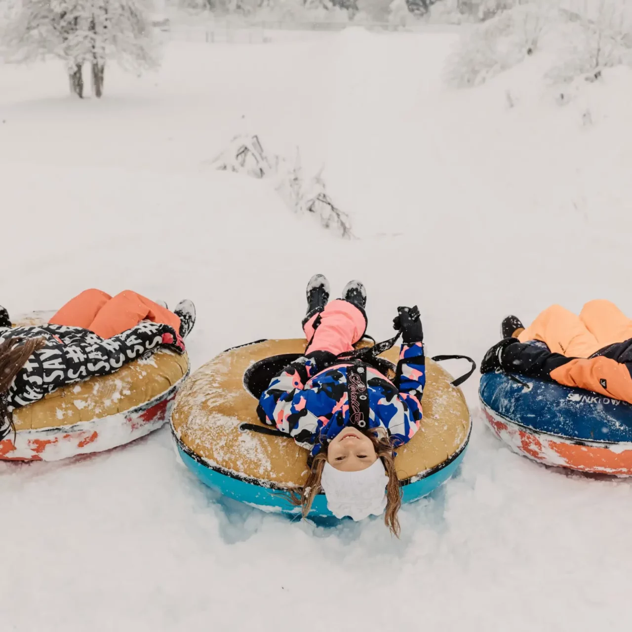 Three children laughing on snowtubes in the snow - pure winter joy and tobogganing fun at Hofgut Wagrain.