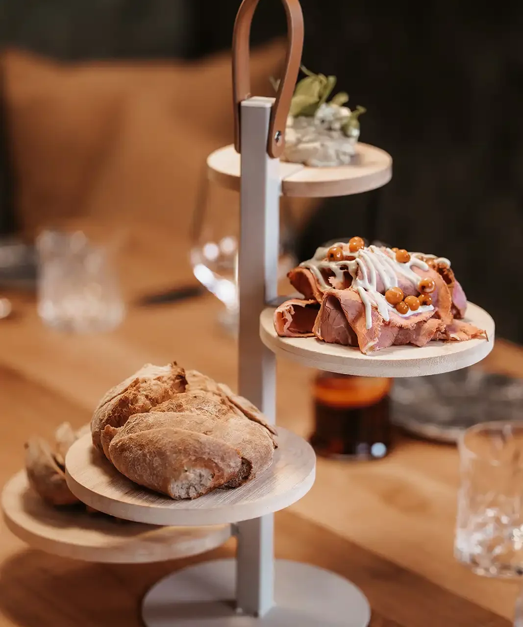Ein mehrstöckiger Servierständer im Restaurant, der verschiedene Brotsorten und mit Sauce bedeckte Fleischscheiben zeigt.