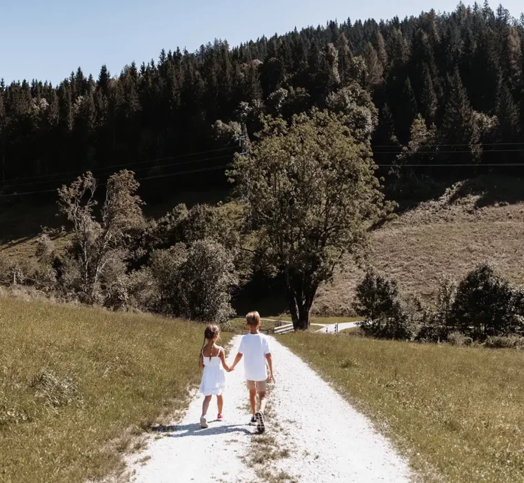 Zwei Kinder spazieren Hand in Hand durch die Natur beim Hofgut Wagrain an einem Sommertag