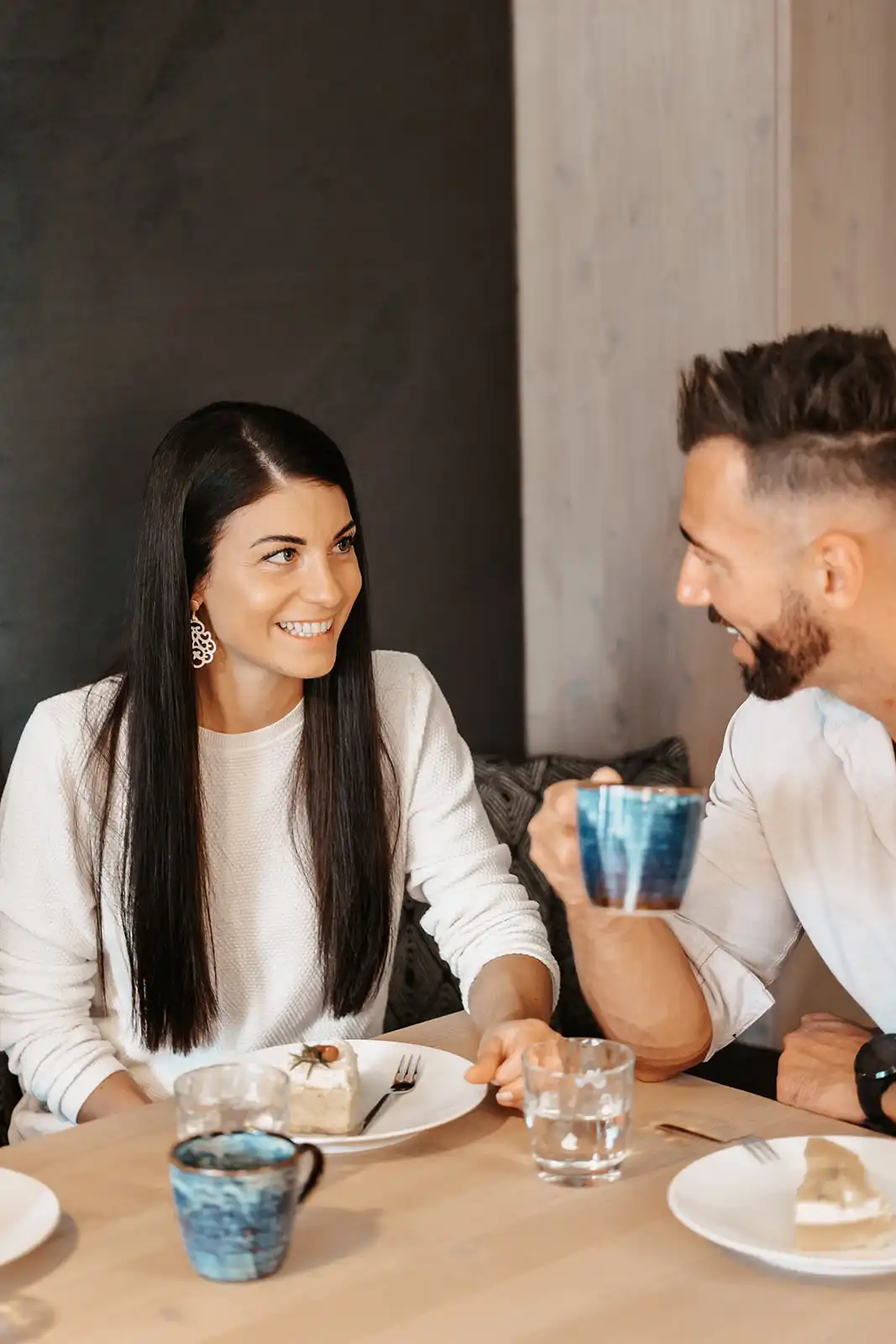 Paar genießt Kaffee und Kuchen in stilvollem Ambiente, während sie sich liebevoll in die Augen sehen.