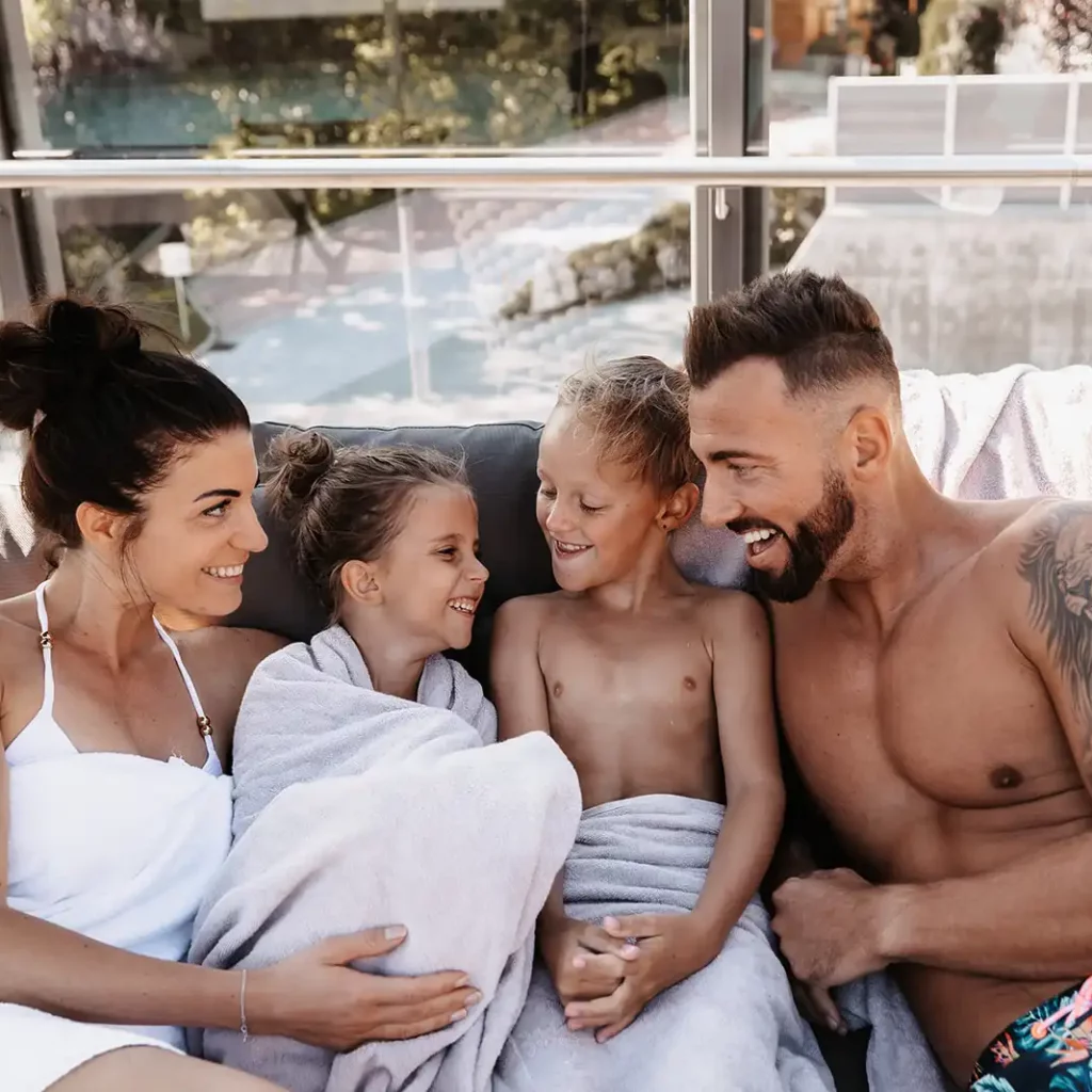 Familie entspannt gemeinsam auf einer großen Outdoor-Liege, eingehüllt in Handtücher, nach dem Badevergnügen.