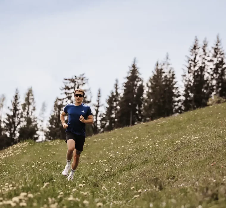 Trailrunners op een alpenweide met een bergpanorama op de achtergrond.