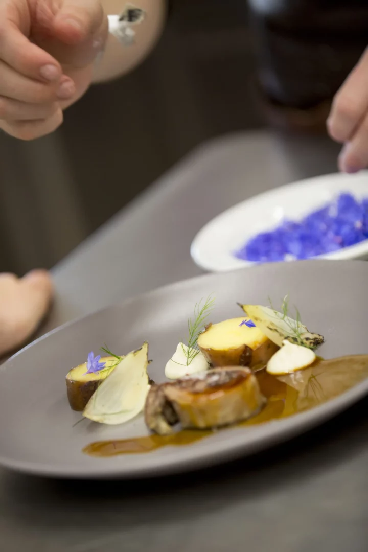 Fein angerichtetes Gourmetgericht mit Kartoffeln, Jus und essbaren Blüten in moderner Fine-Dining-Präsentatio