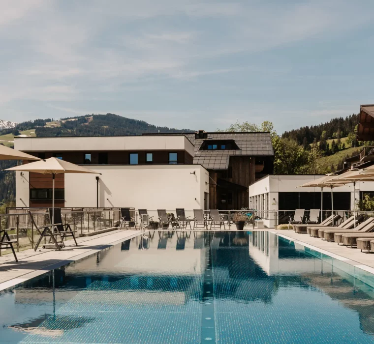 25-metre sports pool at Hofgut Wagrain with sun loungers and umbrellas - summer oasis of peace with mountain views for active and relaxing holidays in Salzburger Land.