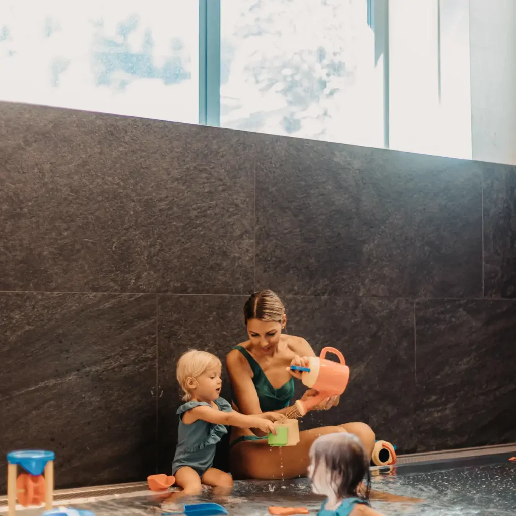 Playtime together in the baby pool - a mother and her two little daughters enjoy the relaxed atmosphere in the warm water area at Hofgut Wagrain, surrounded by loving details and child-friendly water toys.