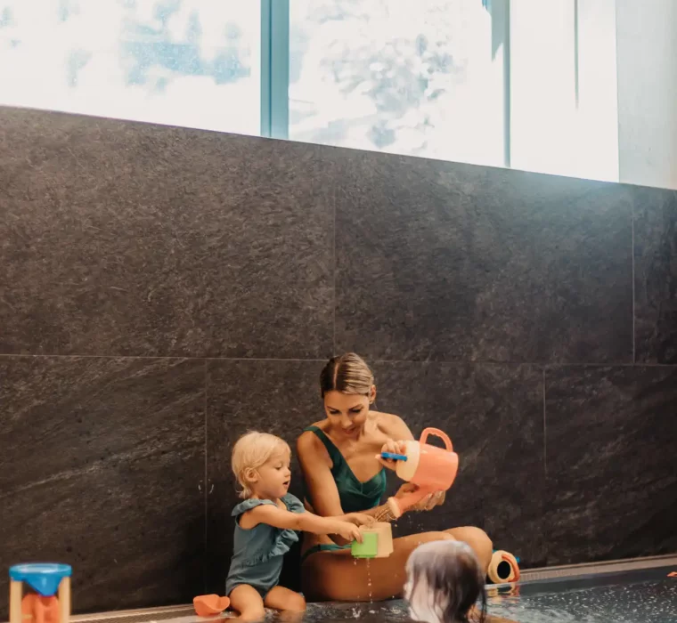 Playtime together in the baby pool - a mother and her two little daughters enjoy the relaxed atmosphere in the warm water area at Hofgut Wagrain, surrounded by loving details and child-friendly water toys.