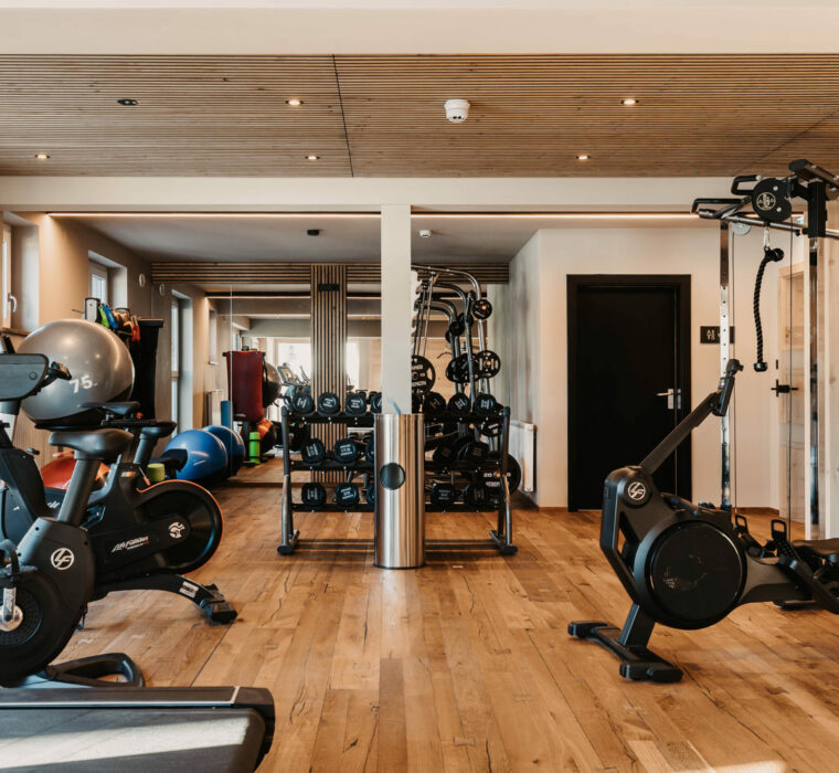 Modernes Fitnessstudio im Hofgut Wagrain mit hochwertigen Geräten, Holzdesign und Blick auf die verschneiten Berge.