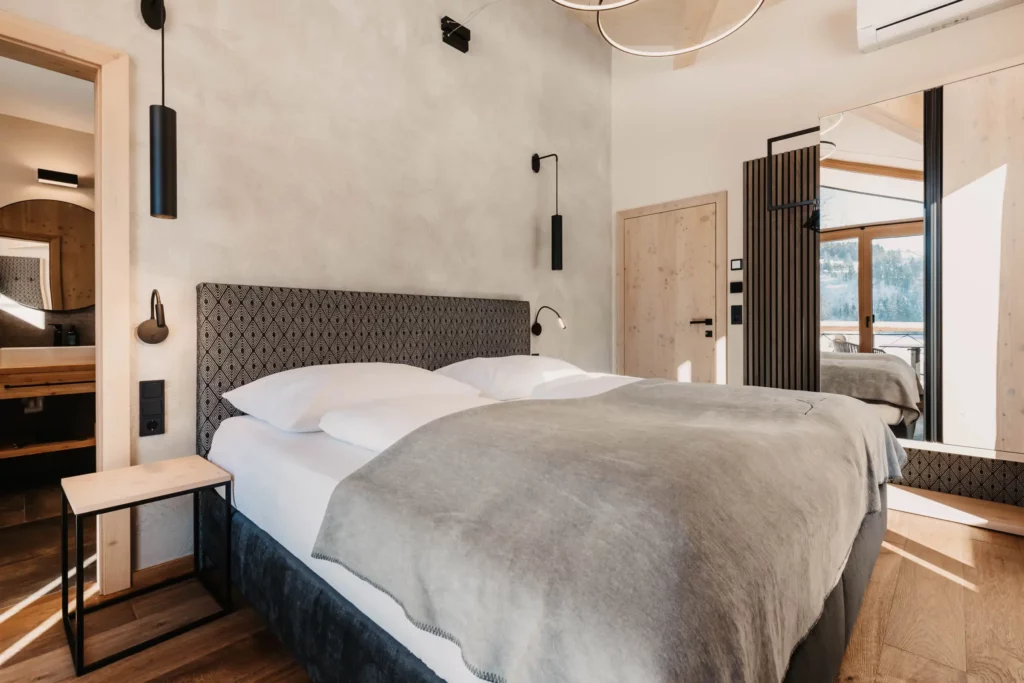 Modern bedroom at Hofgut Wagrain with stylish design, cosy box-spring bed and balcony with mountain view.